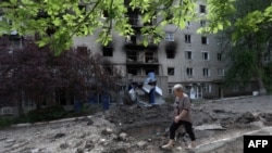 A woman walks past a shell crater in front of a damaged residential building in the town of Siversk, Donetsk region, on June 23, 2022, amid Russia's military invasion launched on Ukraine.