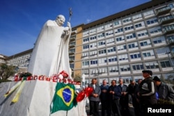 Papa Francis'in tedavi gördüğü Gemelli hastanesinin dışındaki 2005 yılında ölen Papa 2. John Paul'e ait heykelin önünde dua eden insanlar- 23 Şubat 2025.